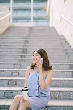 快乐的年轻的亚洲女孩会说话的电话坐着户外楼梯生活方式城市女孩