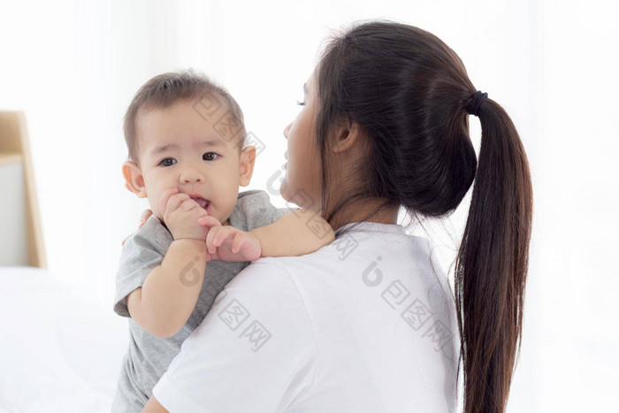 年轻的亚洲妈妈。持有婴儿女孩卧室首页妈妈携带孩子护理女人孩子无忧无虑的蹒跚学步的父情感表达式家庭概念