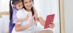年轻的亚洲妈妈女儿视频调用平板电脑电脑问候家庭快乐妈妈。女孩的关系技术沟通互联网在线人