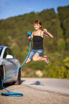美丽的年轻的女孩跳电车持有蓝色的充电电缆