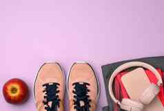 一对粉红色的运动鞋无线耳机智能手机聪明的看紫色的背景