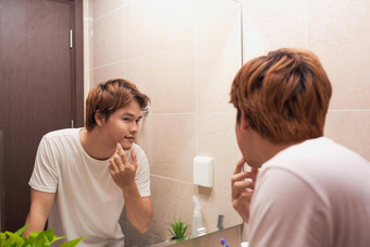 年轻的亚洲男人。镜子检查皮肤浴室