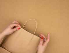女手持有空棕色（的）纸袋处理棕色（的）背景