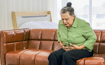 <strong>亚洲</strong>上了年纪的女人持有胃疼痛坐着沙发房间