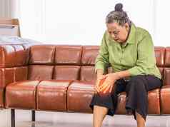 亚洲上了年纪的女人持有膝盖疼痛坐着沙发房间