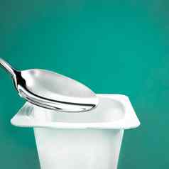 酸奶杯银勺子绿色背景白色塑料容器酸奶奶油新鲜的乳制品产品健康的饮食营养平衡