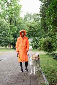年轻的女人橙色雨衣走狗公园