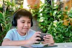 亚洲男孩穿耳机微笑玩游戏聪明的电话