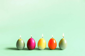 传统的复活节装饰明亮的燃烧石蜡蜡烛形状色彩斑斓的鸡蛋绿色背景