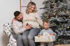 圣诞节家庭幸福肖像爸爸怀孕了妈妈儿子坐着扶手椅首页圣诞节树拥抱微笑