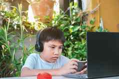 亚洲男孩穿耳机白色衬衫微笑玩游戏聪明的电话