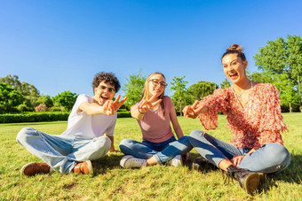 年轻的学生朋友坐着草城市公园显示胜利标志手指相机概念<strong>团结团结</strong>青年年龄快乐基因微笑自然