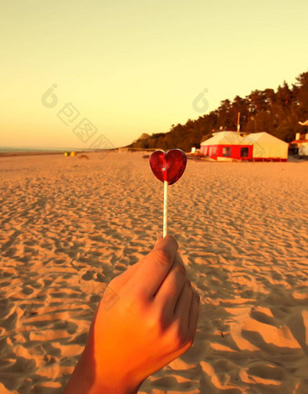 红色的糖果形状心手桑迪海滩背景日落温暖的光垂直拍摄