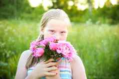 金发碧眼的女孩持有粉红色的新鲜的牡丹花
