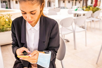 年轻的女人企业家发短信智能手机坐着酒吧外面持有保护脸面具手自由女孩采取早餐酒店咖啡馆技术正常的习惯