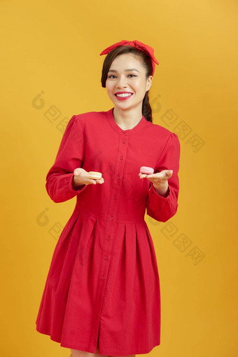年轻的亚洲女人孤立的黄色的背景持有色彩斑斓的法国马卡龙吃