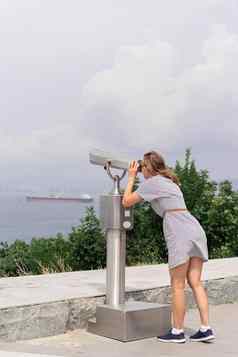 年轻的女人静止的双筒望远镜温暖的夏天一天山背景海城市