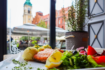 烤大马哈鱼被捣成糊状的土豆柠檬西红柿红色的洋葱橄榄沙拉叶子背景历史建筑孙子波兰餐厅表格窗口
