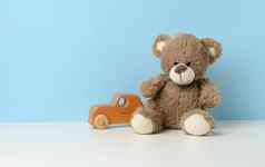 可爱的棕色（的）泰迪熊坐在白色表格木孩子们的玩具车蓝色的背景