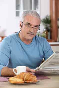 中年男人。阅读报纸同时吃早餐