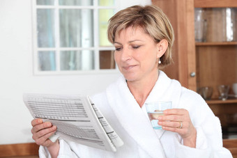 女人浴袍阅读报纸喝玻璃水