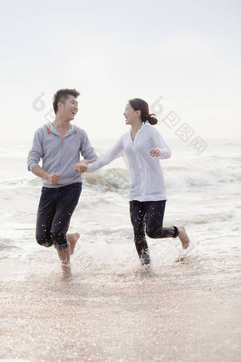 年轻的夫妇持有手运行水域边缘海滩中国