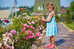 可爱的女孩蓝色的衣服浇水花软管花园
