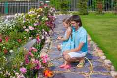 可爱的女孩年轻的父亲浇水花软管花园