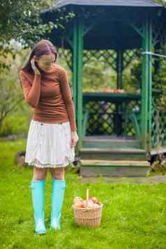 年轻的女孩橡胶靴子篮子红色的苹果花园背景木阿伯