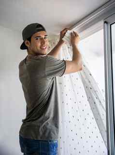 年轻的男人。安装窗帘窗口