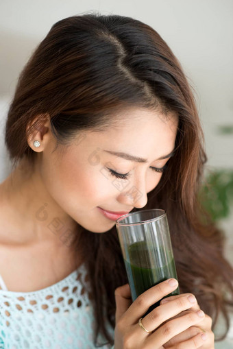 漂亮的年轻的亚洲女人持有绿色新鲜的蔬菜汁