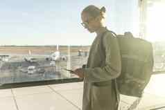 随便穿着女旅行者机场聪明的电话设备前面机场门窗户俯瞰飞机机场跑道