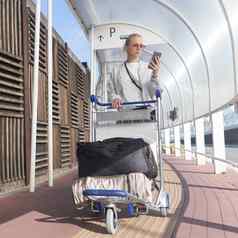年轻的休闲女人移动电话应用程序运输行李到来停车国际机场离开termainal行李电车