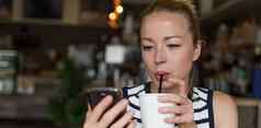 深思熟虑的女人阅读新闻移动电话喝着咖啡咖啡商店