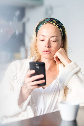 美丽的高加索人女人首页感觉舒适的穿白色浴袍采取时间喝早....咖啡阅读新闻移动电话设备早....