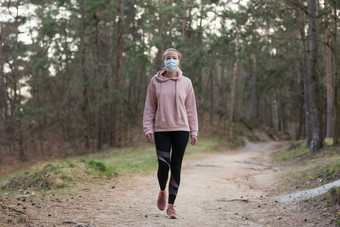 电晕病毒科维德传播世界肖像高加索人运动女人穿医疗保护脸面具走森林电晕病毒