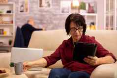 上了年纪的女人坐着沙发数字平板电脑舒适的生活房间