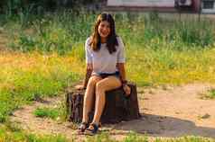 美丽的浅黑肤色的女人女孩白色衬衫蓝色的牛仔裤短裤坐在树桩公园