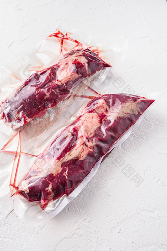 一对查克卷牛肉牛排真空包装有机肉下面请参阅烹饪白色混凝土变形背景一边视图