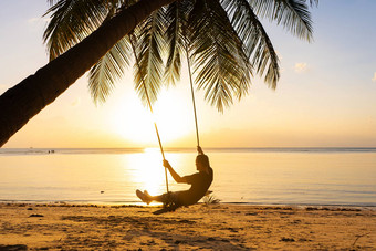 的家伙享受日落骑摇摆不定的热带海滩轮廓的家伙摇摆不定的挂棕榈树看日落水