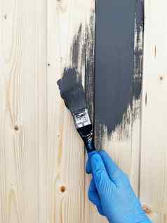 手工人蓝色的橡胶手套油漆木墙刷灰色的油漆
