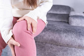 年轻的女人痛苦膝盖疼痛坐着沙发首页医疗保健医疗每天生活概念