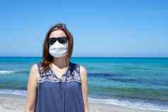 冠状病毒海边假期女人站沙子海滩相机面具科维德流感大流行