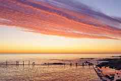橙色红色的天空华丽的云被遗弃的海码头黎明日落水反射岩石