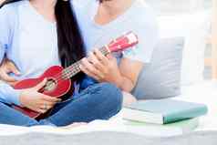 年轻的亚洲夫妇玩尤克里里琴放松幸福