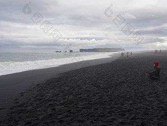 南冰岛维克米达尔7月年轻的漂亮的女人红色的他坐着冥想放松trysfjara黑色的沙子海滩迪霍莱岩石集团旅游人背灌雾喜怒无常的天空单色