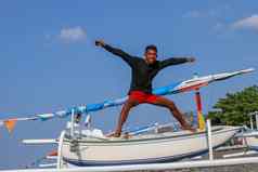 快乐年轻的男人。跳海滩年轻的快乐的印尼跳跃少年好情绪跳跃空气背景钓鱼船阳光明媚的热带一天蓝色的天空