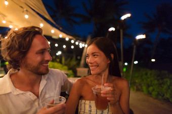 夫妇约会喝酒吧晚上户外餐厅阳台夏威夷假期旅行亚洲女人男人。有趣的敬酒五月或饮料夏威夷鸡尾酒奢侈品生活方式