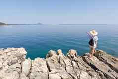 女人旅行者穿稻草夏天他背包站边缘岩石悬崖指出大蓝色的海岛屿地平线