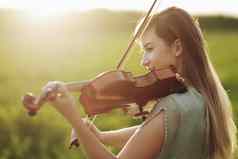 浪漫的女人宽松的头发玩小提琴日落光自然